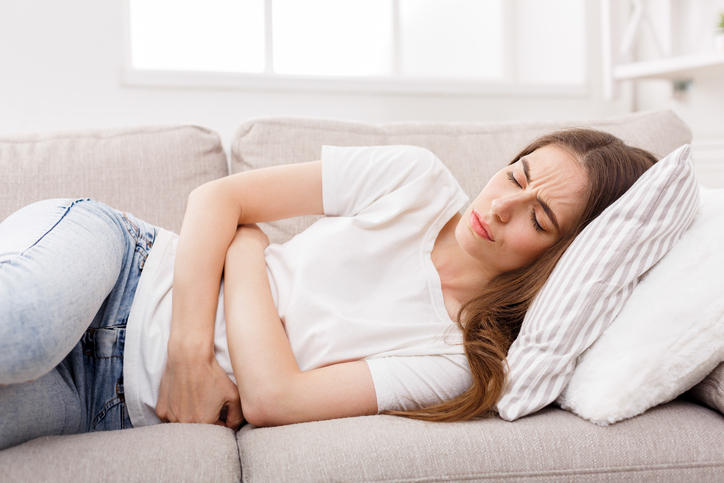 young woman suffering from stomachache lying on couch at home, copy space